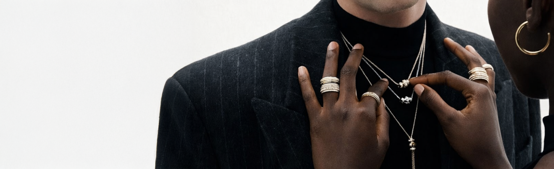 Personne portant plusieurs colliers fins et bagues en argent superposés avec tenue élégante, style luxe et raffiné